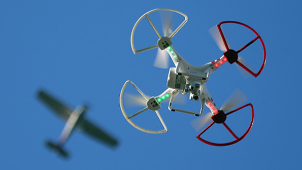 A quadcopter drone hovers far below a commercial airliner