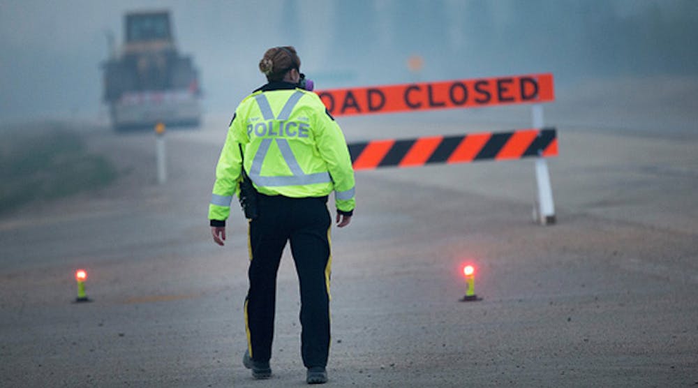 Smoke fills the air as a police officer stands guard at a roadblock leading into Fort McMurray on May 8, 2016. Wildfires have forced the evacuation of tens of thousands residents from the town.