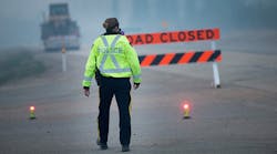Smoke fills the air as a police officer stands guard at a roadblock leading into Fort McMurray on May 8, 2016. Wildfires have forced the evacuation of tens of thousands residents from the town.