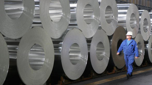 A worker walks past rolls of semifinished aluminum