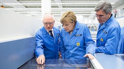 Siemens CEO Joe Kaeser, right, and German Chancellor Angela Merkel, center, listen to Karl-Heinz B&uuml;ttner, head of the Siemens plant in Amberg, discuss a circuit board during a factory tour.