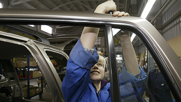 An autoworker installs door panels in a factory