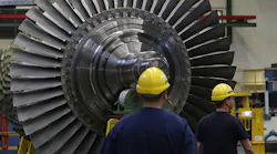 Workers stand near a turbine in a factory