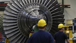 Workers stand near a turbine in a factory Workers stand near a turbine in a factory