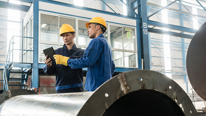 A pair of worker stand over a tablet in a factory.
