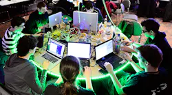 A group of hackers huddle around laptops.