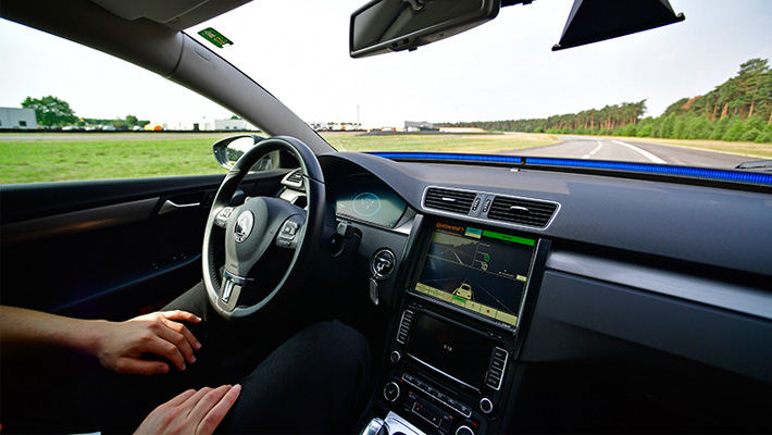 A human sits in an autonomous car, not touching the steering wheel.