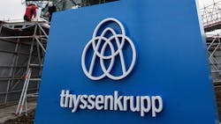The ThyssenKrupp logo and wordmark in front of a German elevator testing tower The ThyssenKrupp logo and wordmark in front of a German elevator testing tower