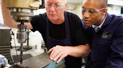 A milling machine worker shows an apprentice how to work the tool.