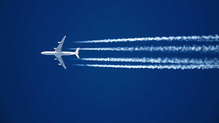 An airplane flies through the sky, leaving trails