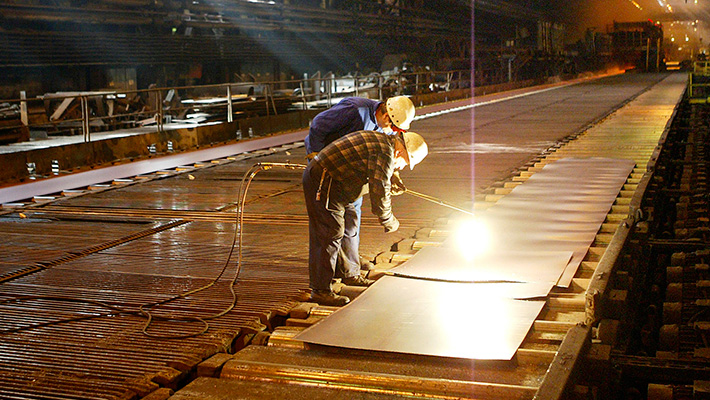 Workers examine hot steel at a mill.