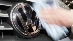 A disembodied hand wipes clean a VW logo on the grille of a car. A disembodied hand wipes clean a VW logo on the grille of a car.