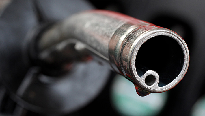 A photo illustration of a gas pump with a single drop hanging from the end of the nozzle.