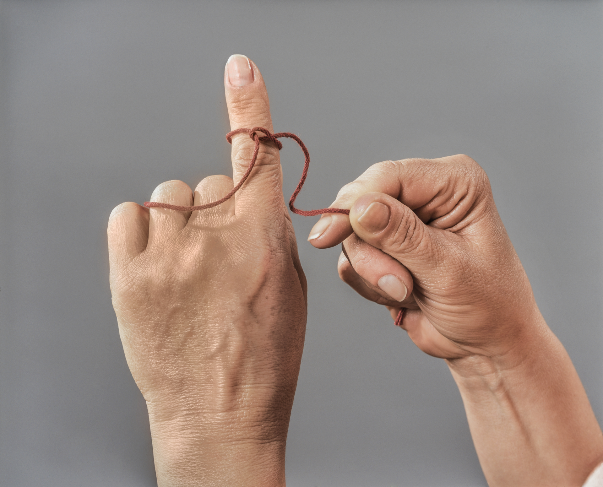 Two hands, one tying a string around index finger of the other