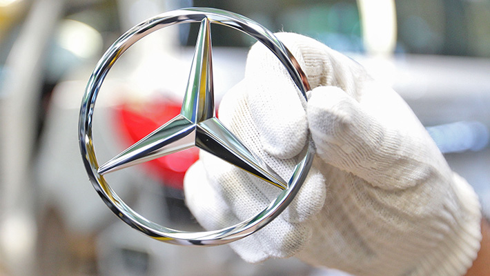A gloved hand holds a Mercedes-Benz logo hood ornament.