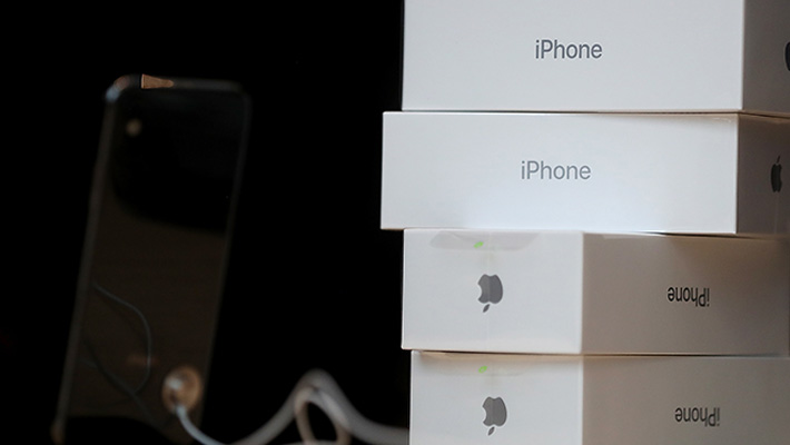 A pile of Apple iPhone X boxes next to a new phone on display.