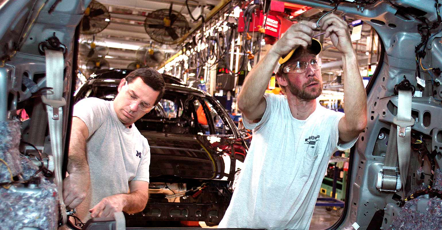 2 Ford workers affixing components on a vehicle
