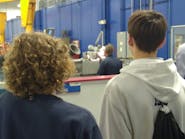 Two Benedictine students pause on their way around SKF&rsquo;s factory floor to watch an employee at work.