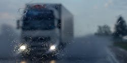 A freight transportation truck drives on a highway in the rain.