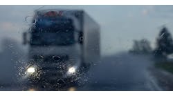 A freight transportation truck drives on a highway in the rain.