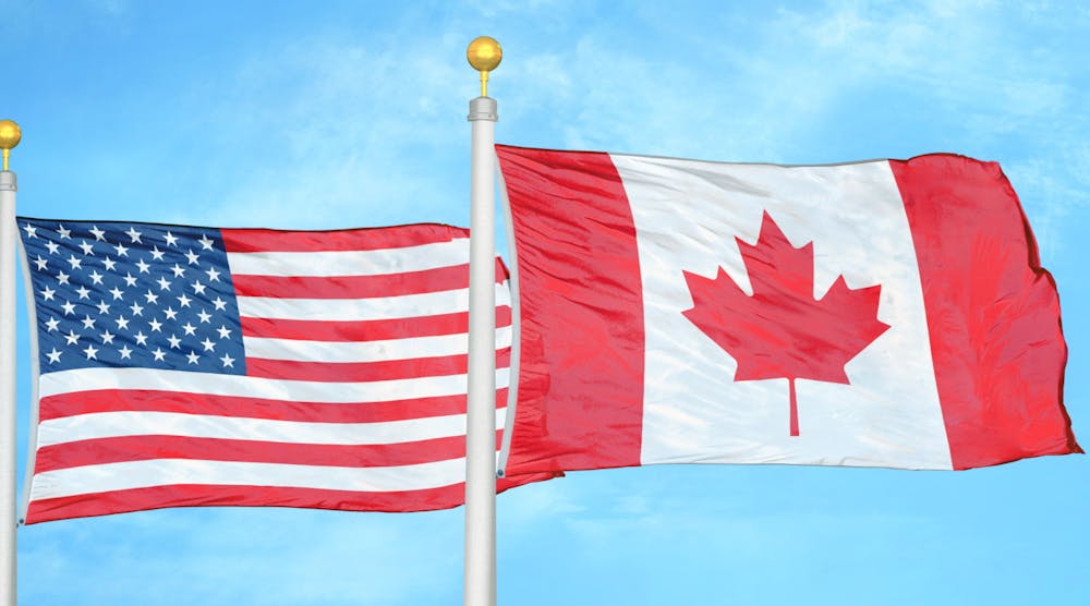 The flags of the United States and Canada flying side-by-side against a blue sky.