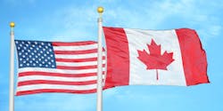 The flags of the United States and Canada flying side-by-side against a blue sky. The flags of the United States and Canada flying side-by-side against a blue sky.