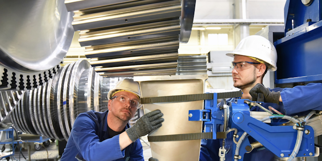 Two workers in hard hats and eye protection assemble a steel turbine.