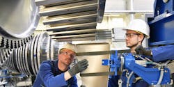 Two workers in hard hats and eye protection assemble a steel turbine. Two workers in hard hats and eye protection assemble a steel turbine.
