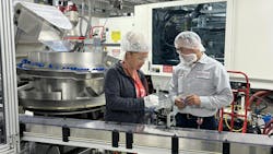 Two people in hairnets inspect parts on manufacturing floor. Two people in hairnets inspect parts on manufacturing floor.