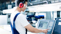 Man programming CNC machine on factory floor. Man programming CNC machine on factory floor.