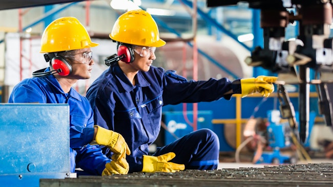 Workers in factory at industrial metal cutting machine.