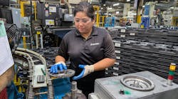 Machine operator Rebecca Asuncion removes a finished part from an outbound conveyor to be placed onto a digital check fixture to then be packed into finished goods. Machine operator Rebecca Asuncion removes a finished part from an outbound conveyor to be placed onto a digital check fixture to then be packed into finished goods.