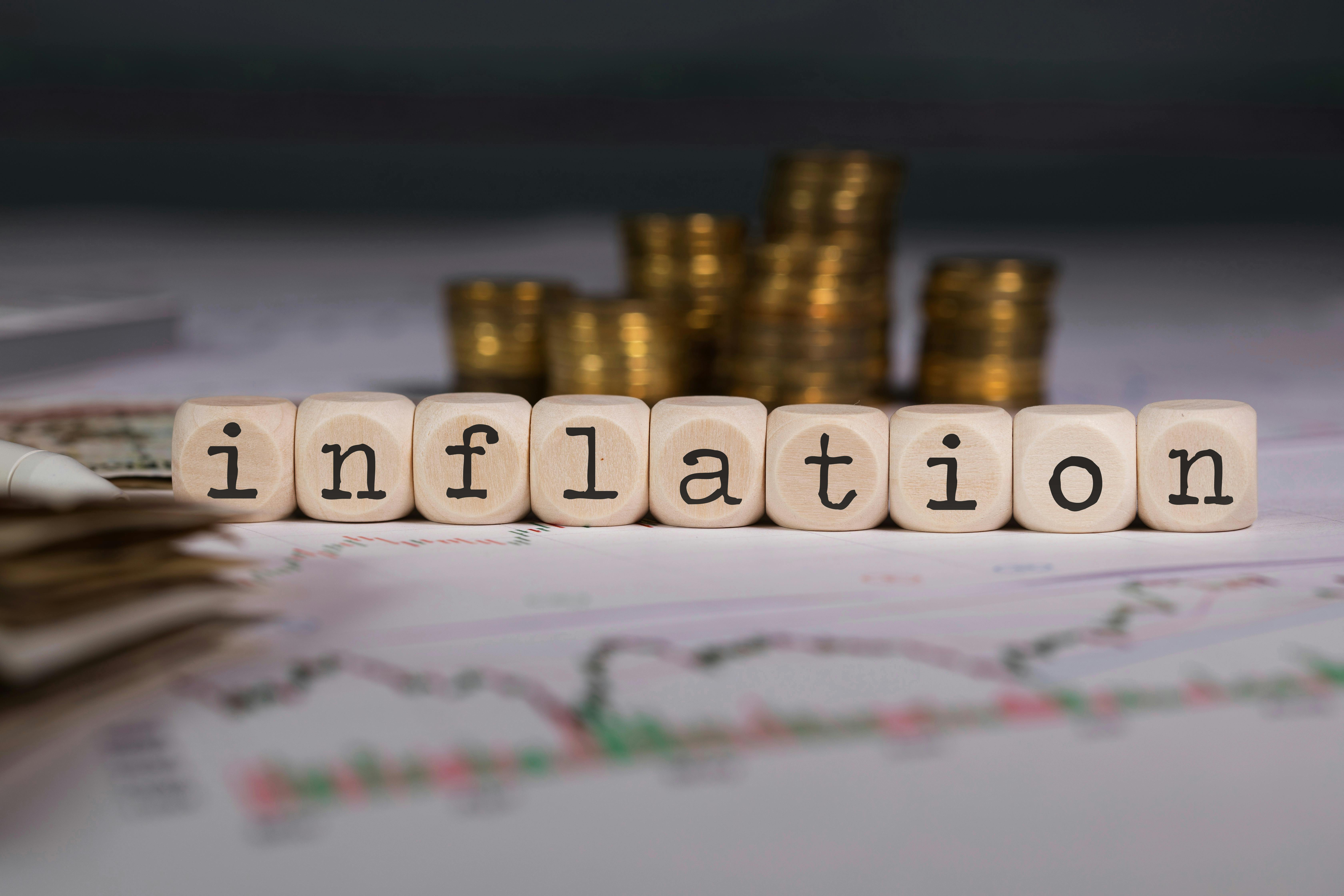 Word INFLATION composed of wooden letters. Stacks of coins in the background