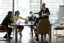Company executive giving papers to employees at group meeting Company executive giving papers to employees at group meeting