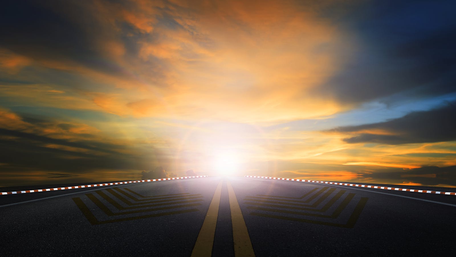 sun rising in the sky above an asphalt highway.