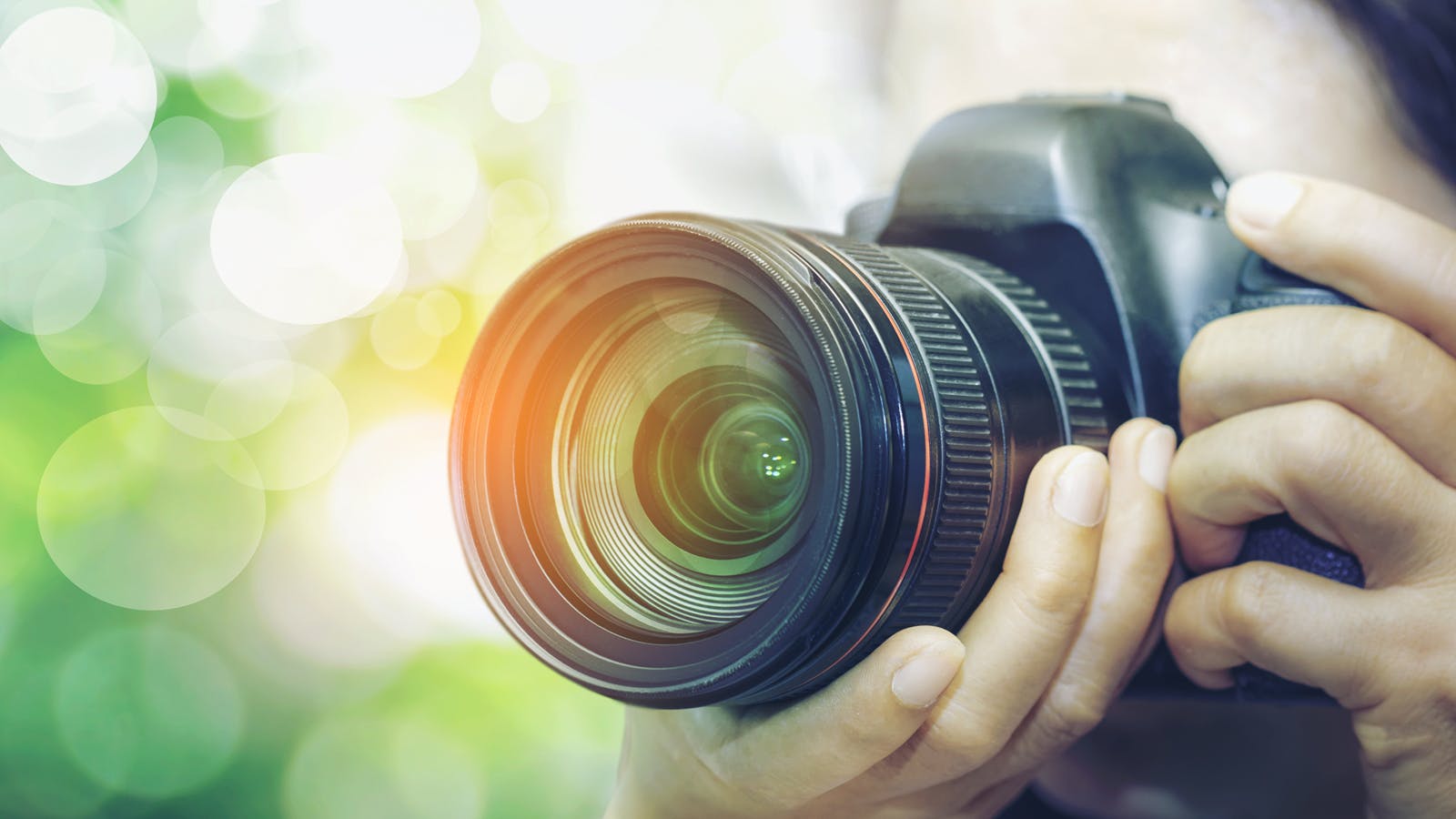 hands holding a camera and aiming at something off the screen. Green background.