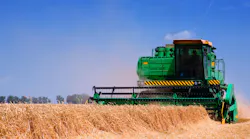 Green farm equipment harvesting wheat in a field with a blue sky background Green farm equipment harvesting wheat in a field with a blue sky background