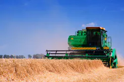 Green farm equipment harvesting wheat in a field with a blue sky background Green farm equipment harvesting wheat in a field with a blue sky background