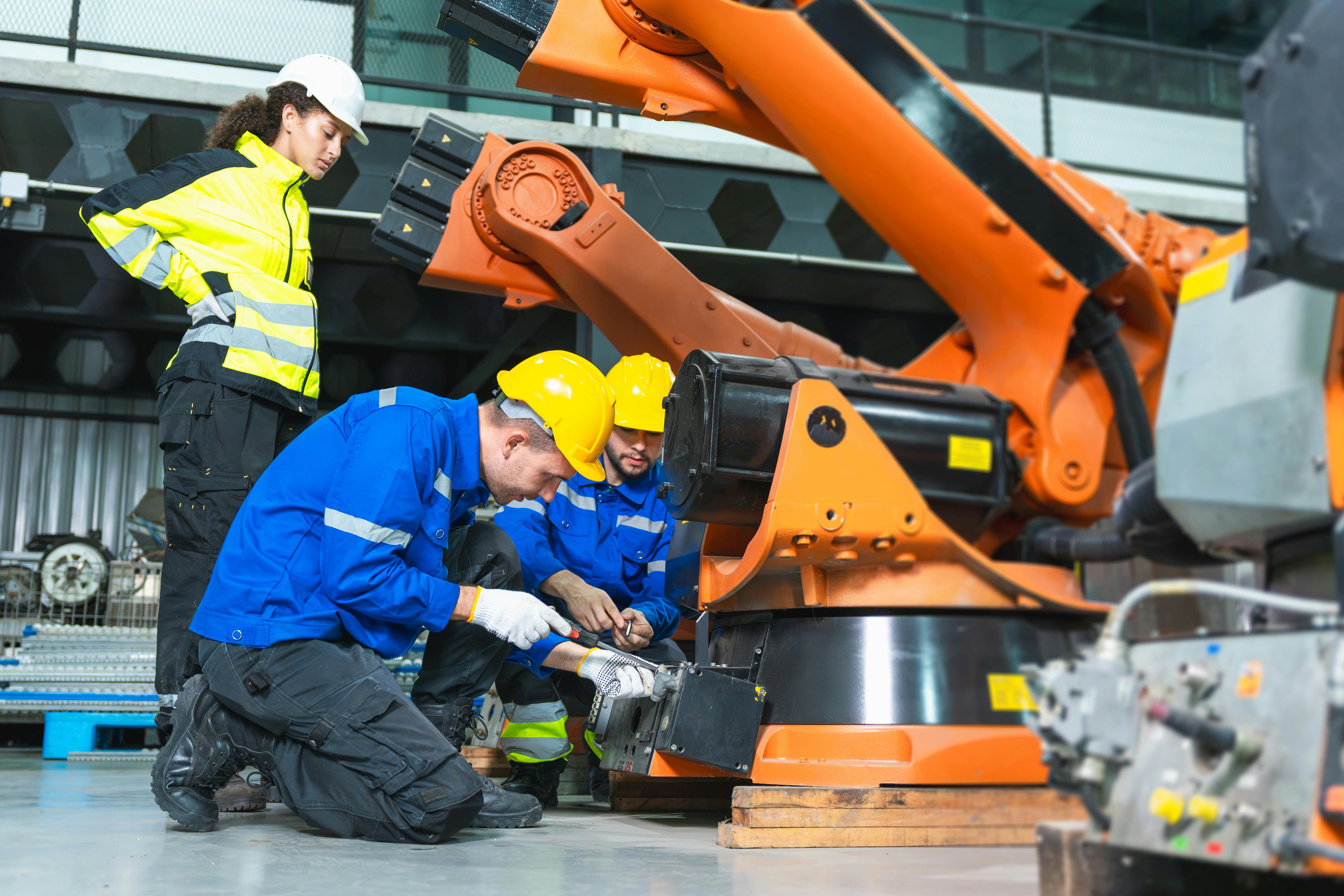 Robotics engineer and technician repairing industrial robot arm in factory